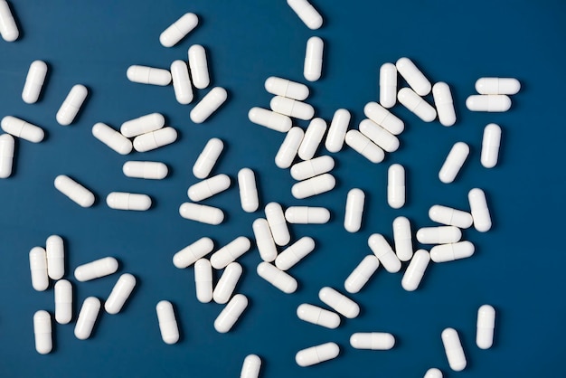 White Drug Capsules Scattered on Blue Table Top View