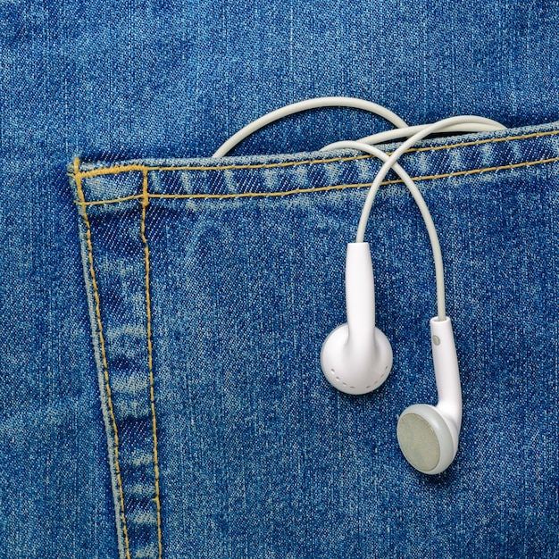 청바지 주머니에 매달려 있는 흰색 이어폰. 현대 이어폰.
