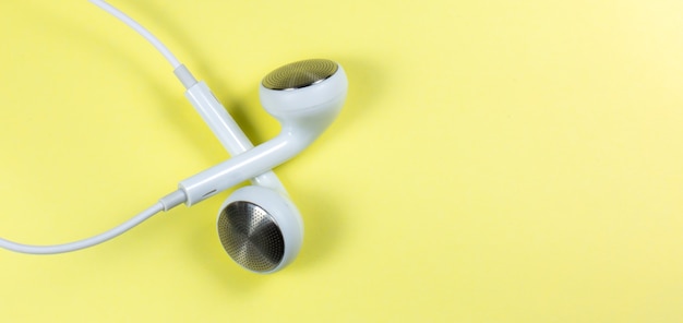 White Earphones lying on the yellow background. Modern music concept. Audio technology. Close up photo.