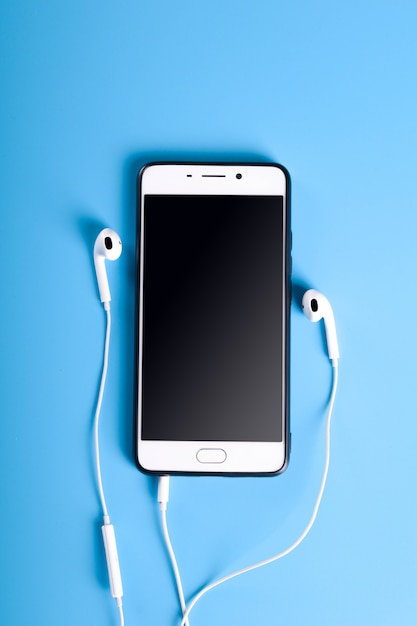 White earphones and smartphone on blue table, top view