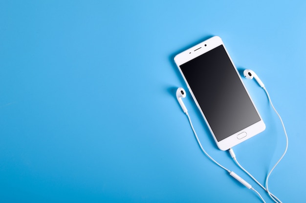 White earphones and smartphone on blue table