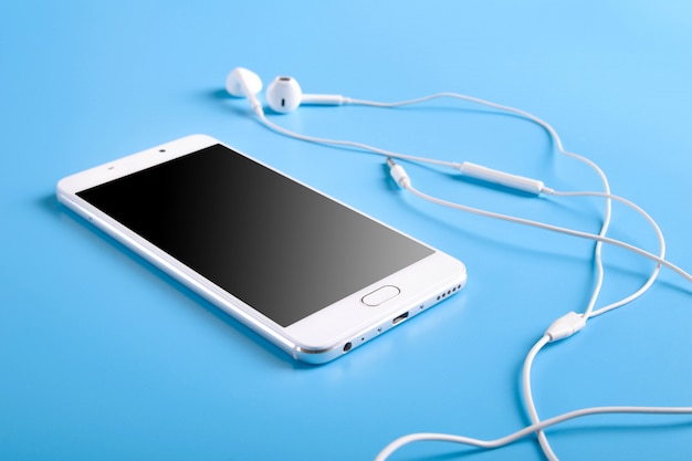 White earphones and smartphone on blue table