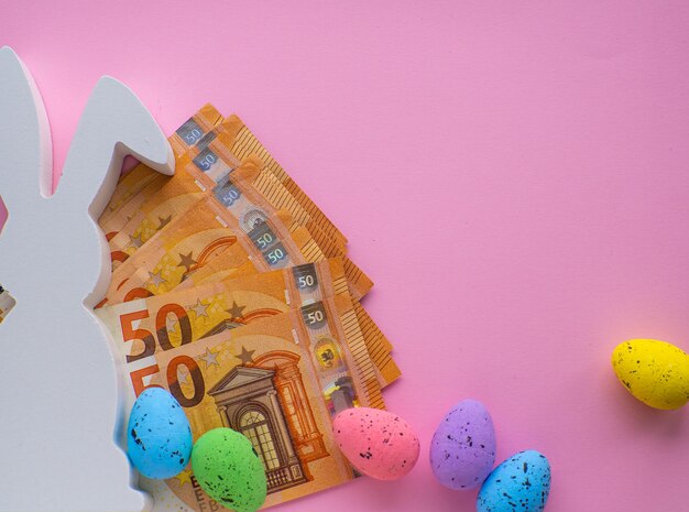 White Easter bunny on Euro banknotes with colorful eggs on pink background