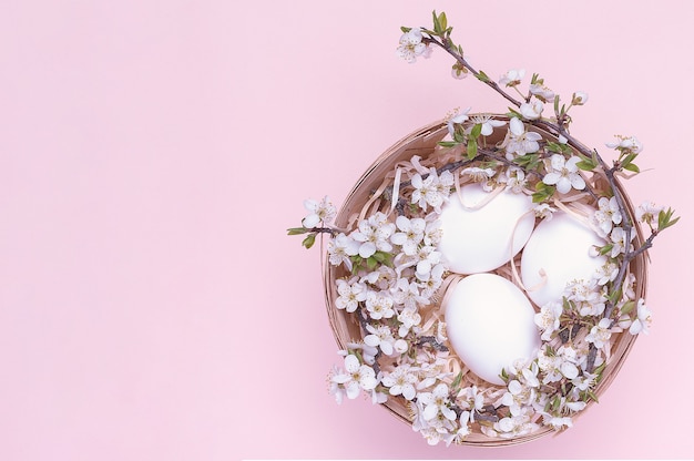 White easter eggs in a basket with flowers on a pink background.