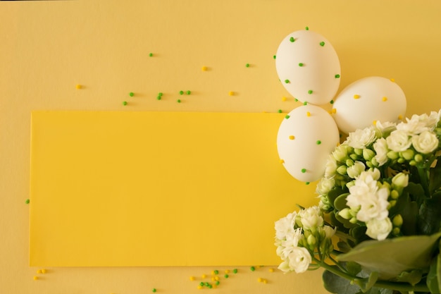 White Easter eggs with polka dots on a yellow background with a bouquet of flowers.