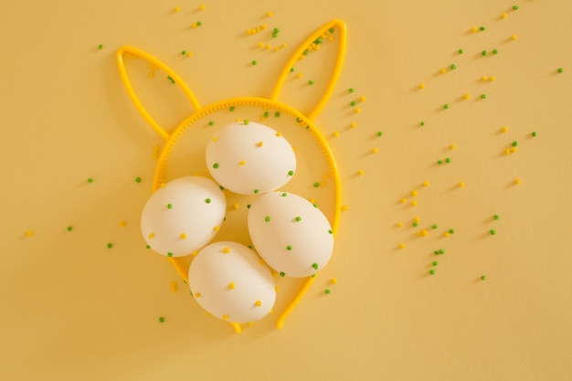 White Easter eggs with polka dots on a yellow background with bunny ears.