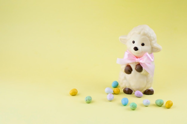 White Easter sheep figure made of white chocolate with small chocolate eggs on yellow background