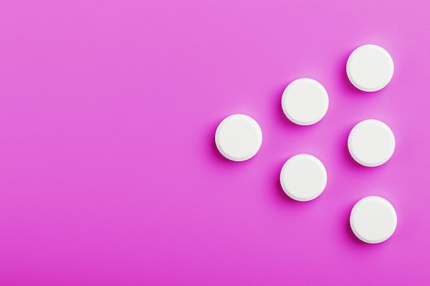 White ecstasy pills in a row on a pink surface isolate