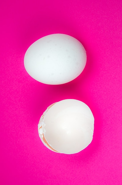 写真 ピンクの背景に白い卵と卵の殻。スペースをコピーします。ミニマリズム、オリジナルでクリエイティブな写真。美しい壁紙。イースター休暇。