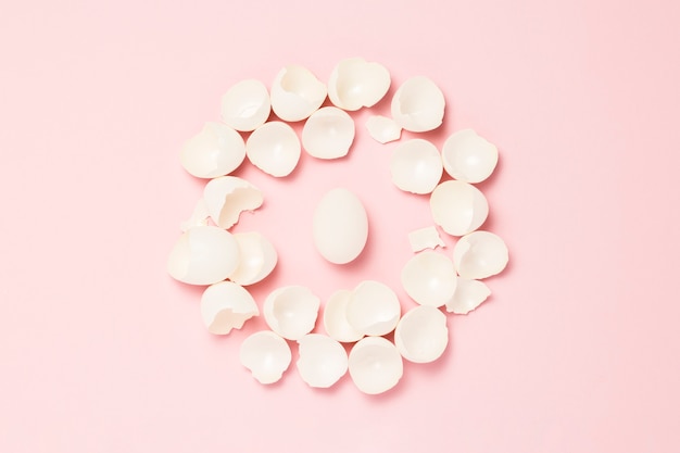 White egg and broken eggs around it on a pink background. concept of life insurance, health and property, waiting for the birth of a child. Flat lay, top view.