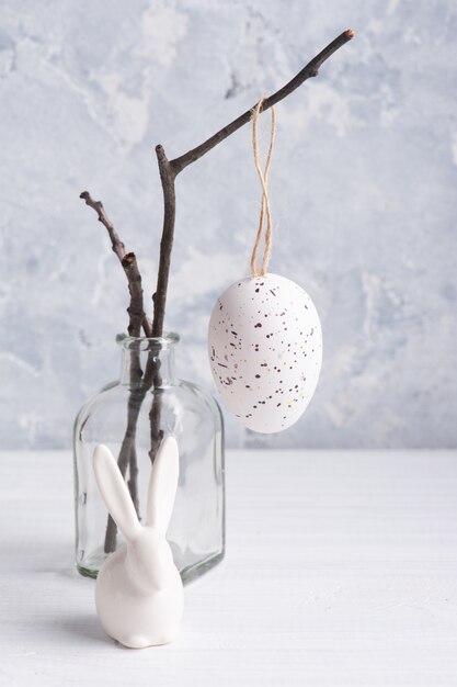 White egg and bunny in rustic Easter composition on white wooden table.