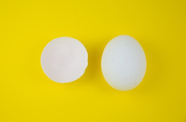 White egg and eggshell on the yellow background. Copy space. Minimalism, original and creative photo. Beautiful wallpaper. Easter holidays.