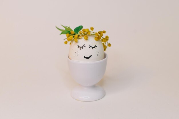 A white egg with a face made of flowers sits in an egg shell with a yellow flower on it.