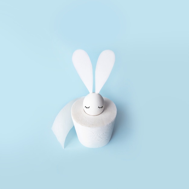 White egg with hare ears in a roll of toilet paper. Hard shadow on a light background. Concept on Easter 2020.