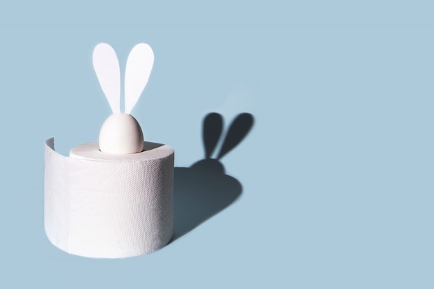 White egg with hare ears in a roll of toilet paper. Hard shadow on a light background.