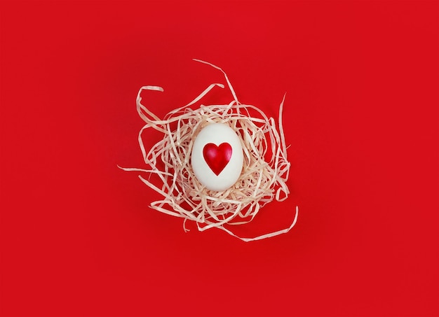 White egg with heart shape in decorative nest on red