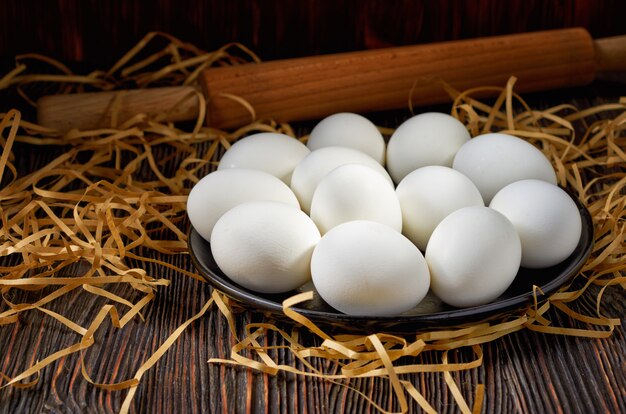 White eggs on a black plate, paper straw and wooden table. On the back of the rolling pin. Restrained.