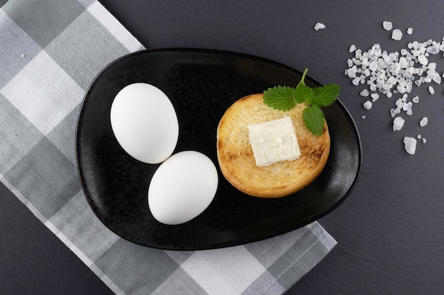 Foto uova bianche in un piatto nero e una fetta di pane tostato caldo con burro concetto di colazione vista superiore