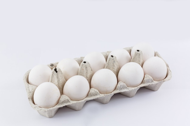 Белые яйца курицы в безвредной картонной упаковке на белом фоне.