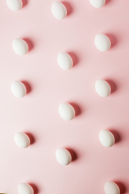 White eggs on a light pink background with reflection of the shadows and copy space