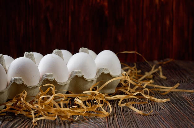 White eggs in a pack on paper straw and wooden table. Low key.