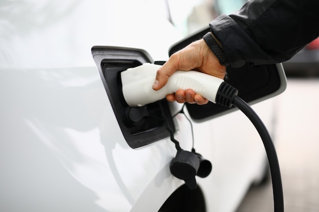 白い電気自動車は充電ステーションで再充電されます。