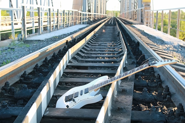White electric guitar on the railroad tracks and industrial gray stone