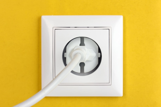 White electric socket with plug on the wall