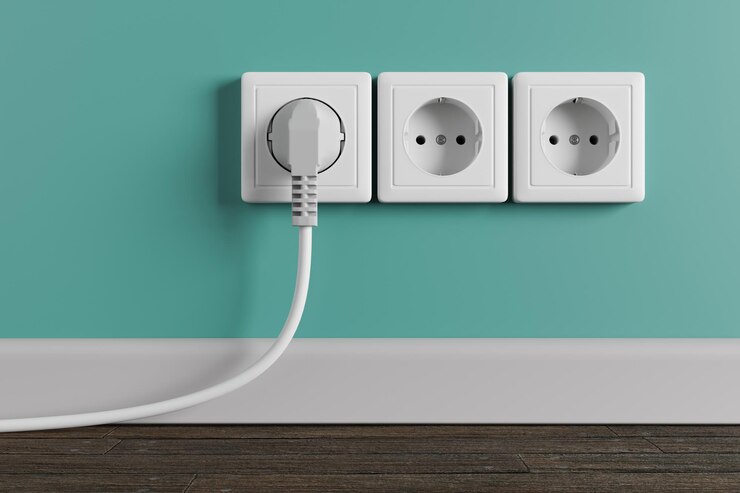 部屋の壁にある白いコンセント。ソケットにケーブルが入った電気プラグ。