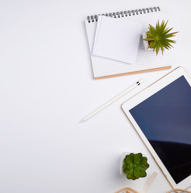 White electronic tablet with a blank screen and a pencil, near pots with green plants