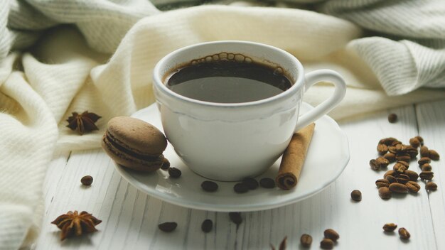 White elegant cup on saucer filled with black coffee and composed on white wooden table with spices