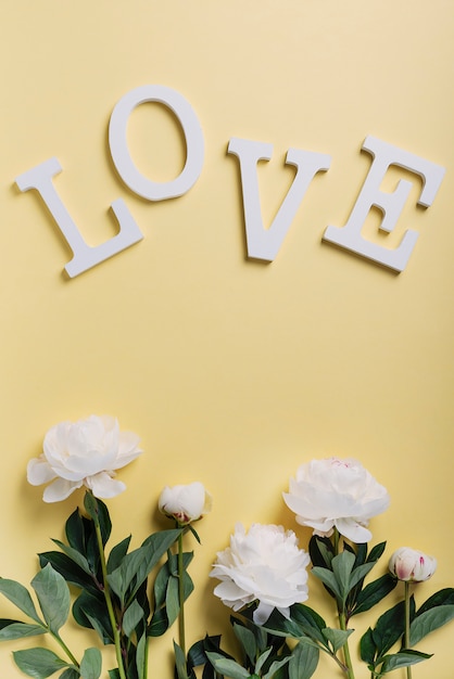 White elegant peonies on the yellow wall and word love