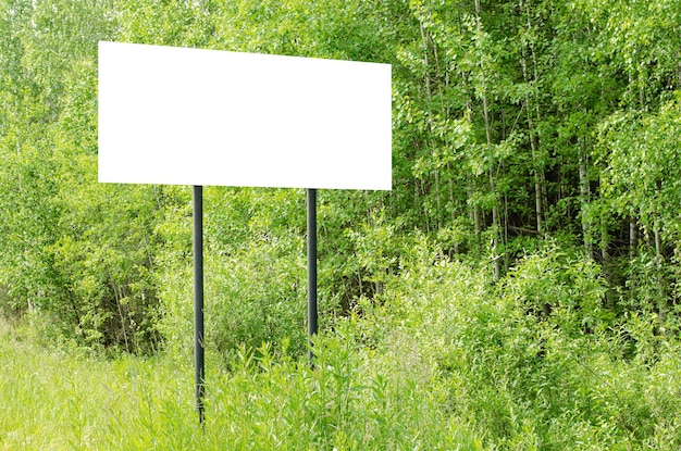 A white empty billboard in the forest among the trees Posting information in a public park or drawing attention to environmental issues Summer copy space