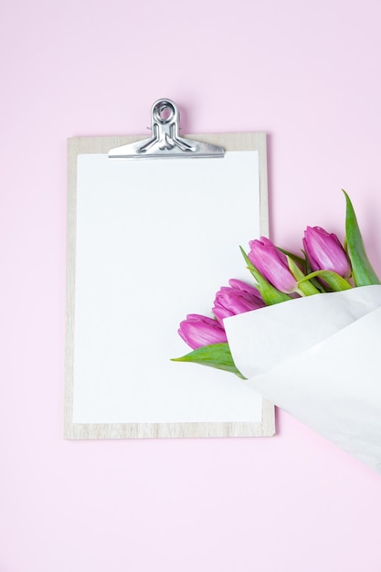 White empty blank purple tulips and a cup of coffee on a pink background Top view flat lay