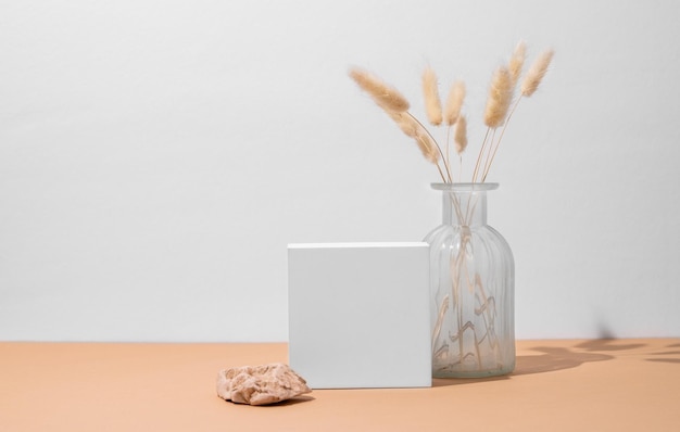 White empty box and vase with dried flowers on a beige background with a hard shadow