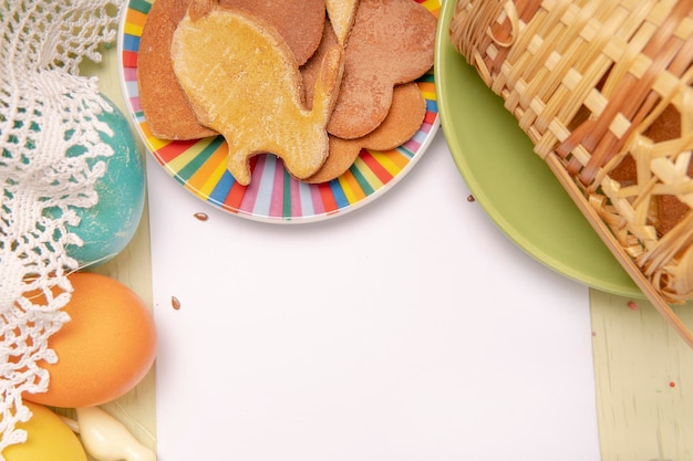 Foto lista bianca vuota sullo sfondo di pasqua con uova colorate e biscotti fatti in casa