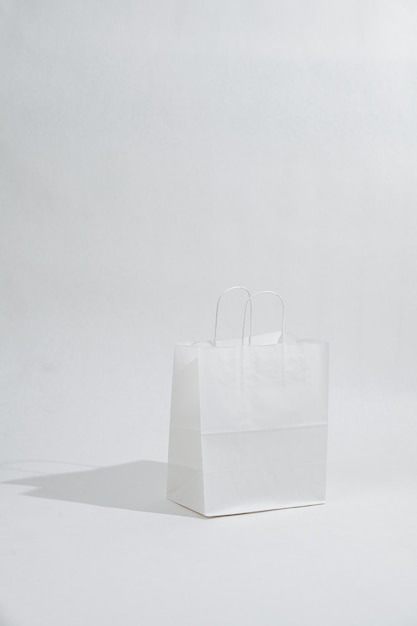 Фото Белый пустой бумажный пакет с веревочными ручками, отбрасывающий тень на белый фон