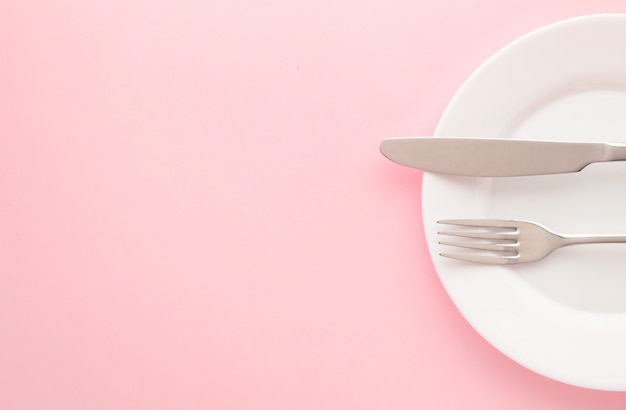 White empty plate with fork and knife on a pink table