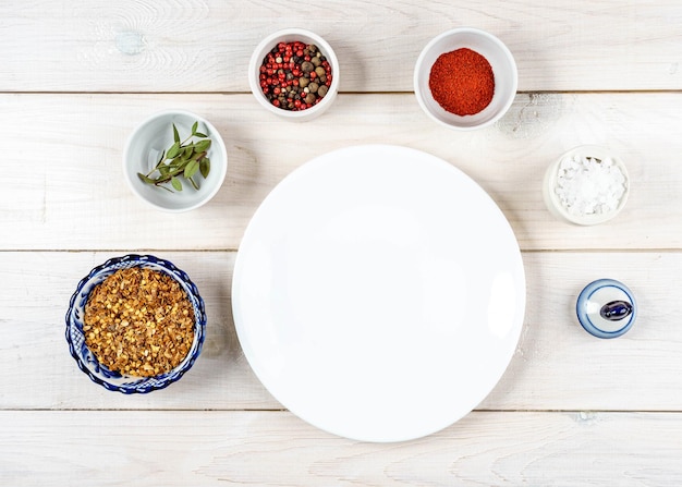 White empty plate on a wooden table with a set of spices around top view