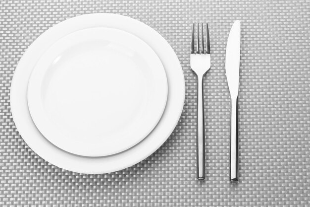 White empty plates with fork and knife on a grey tablecloth