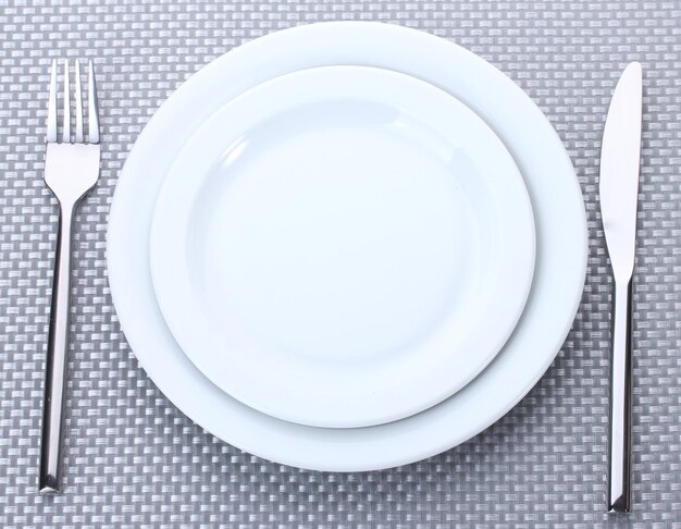 White empty plates with fork and knife on a grey tablecloth