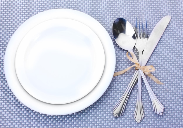 White empty plates with fork spoon and knife tied with a ribbon on a grey tablecloth