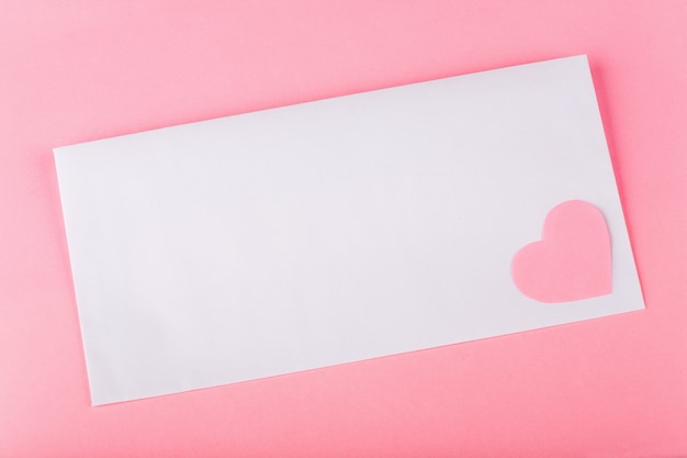White envelop with pink paper heart and space for your text on pink background.