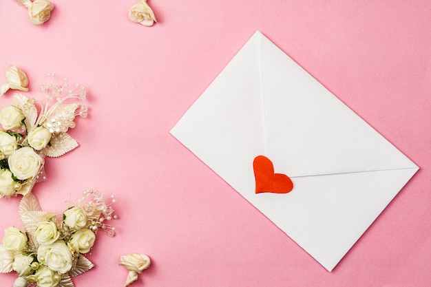 White envelope decorated with a heart and white flowers on a pink surface