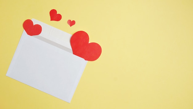 White envelope with flying hearts on a yellow background. Top view.