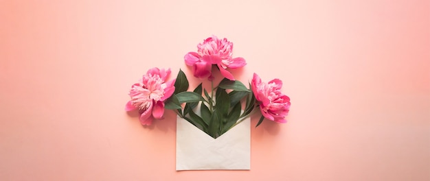 White envelope with pink peonies inside on a pink background template for newsletters and other mail