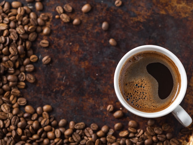 Tazza di caffè espresso bianco e fagioli arrostiti sul vecchio tavolo marrone arrugginito