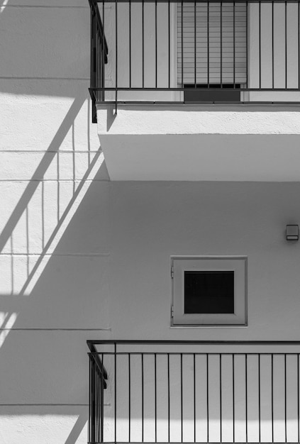 White facade of a flat building with minimalist design and\
small windows the shadow of the black railing is projected on the\
wall looking like stairs