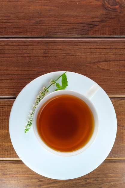 White faience cup with black tea on a saucer on a brown wooden background close-up