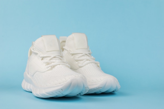 White fashionable fitness sneakers on a blue background. Fashionable sports shoes.